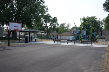 A basketball court with one hoop with a playground behind it