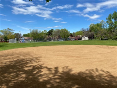 A ballfield with a large grass field behind it