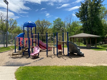 A playground set with a picnic shelter behind it