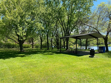 A picnic shelter that sits next to a large green lawn dotted by trees