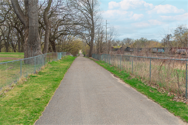 A paved trail alongside a set of train tracks separated by a fence
